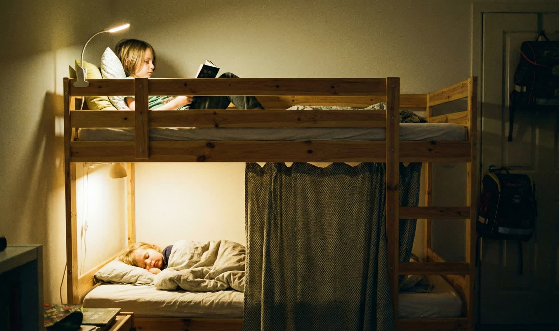 Sosnowe łóżko piętrowe wieczorem: górne piętro do czytania przy lampce, dolne jako zasłonięta norka do snu